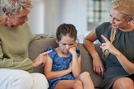 家庭、纪律和母亲和祖母对女孩在家里沙发上的不良行为的手势示意。