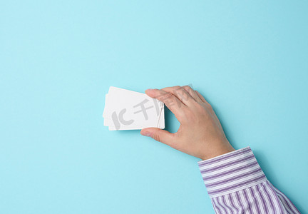 女性手拿着蓝色背景上的空纸白色名片。