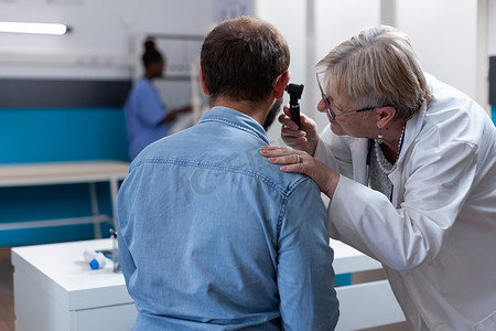 全科医生使用耳镜咨询耳朵，为患者进行健康检查