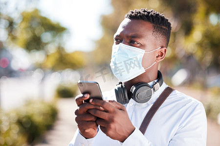 面目全非的黑人戴着口罩，保护自己免受日冕病毒大流行的影响，同时戴着耳机，用手机发短信。
