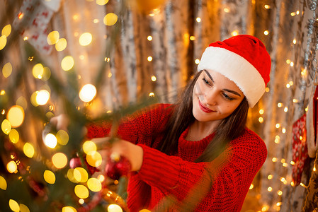 一个戴着圣诞帽、把圣诞装饰品挂在圣诞树上的快乐女孩的照片