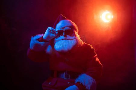 庆祝霓虹灯摄影照片_戴着墨镜的圣诞老人在黑色背景的霓虹灯下。