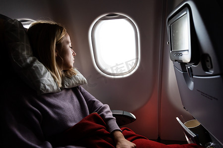在飞机上睡觉摄影照片_疲惫的金发休闲白种女士在乘飞机旅行时睡在座位上。