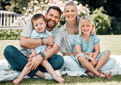 家庭时间摄影照片_阳光明媚的日子里，一个白人家庭坐在后院的毯子上微笑的肖像。