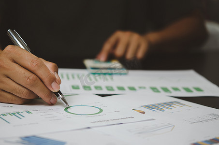 商人手持笔指向文书工作图表报告分析统计和文件财务图表投资营销在公司的办公桌上。