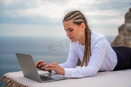 海边躺摄影照片_一位女士躺在露台上，在美丽海景的露台上用笔记本电脑键盘打字。