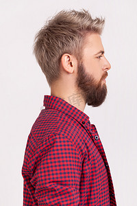 自信的留着胡须的男性的侧面肖像，金发，穿着红色格子衬衫，面容严肃、专注地看着侧面空间