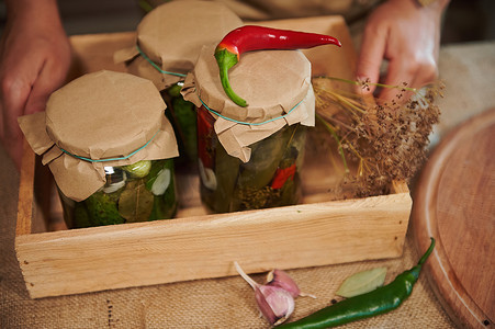 时令蔬菜摄影照片_木箱的裁剪视图，里面装有美味的自制美味腌黄瓜和腌制辣椒的罐子