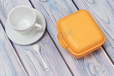 学校餐具摄影照片_塑料黄色午餐盒和杯子与茶碟在木制背景。