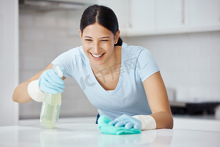快乐的女人清洁家庭厨房，用安全手套喷洒产品清洁剂，并用布擦亮桌子。