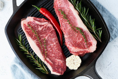 肉条摄影照片_两块新鲜的生大整块肉、牛肉片、大理石西冷牛排放在铸铁大锅里。