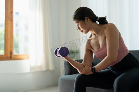 居家锻炼摄影照片_居家锻炼概念 亚洲女性在客厅举重哑铃 隔离期间的心理健康