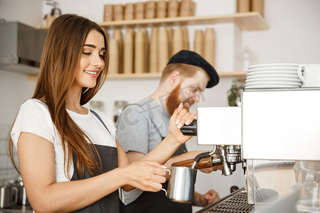 咖啡业务概念-站在咖啡馆时，女咖啡师穿着围裙准备和蒸牛奶，与她的伴侣一起点咖啡。