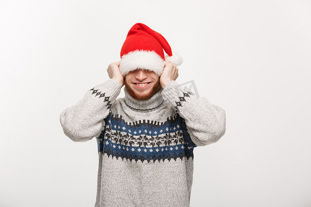假日概念-穿着毛衣的年轻胡子男人喜欢玩圣诞老人的帽子。
