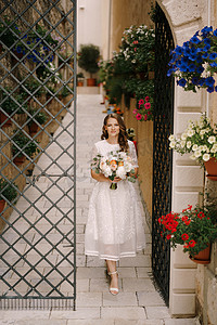 鲜花从摄影照片_带着一束鲜花的新娘从一个有装饰门的老院子里出来