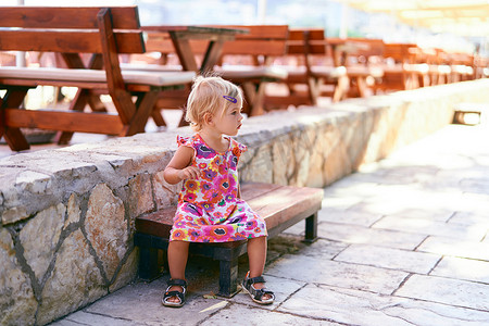 小女孩坐在露天餐厅附近的长凳上