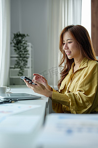 一位女士在办公桌旁休息时使用手机拨打视频电话或给朋友打电话的照片