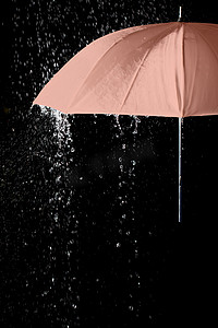 黑色背景雨滴下的粉色雨伞