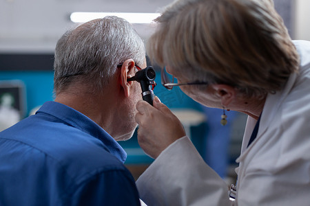 耳镜摄影照片_女医生拿着耳镜为老人在医疗预约时做耳部咨询