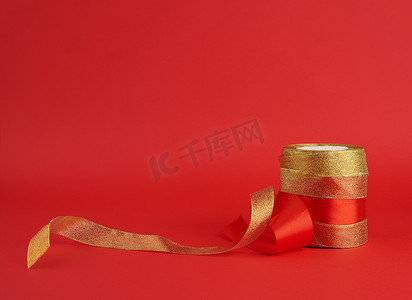 红色背景上扭曲的金色和红色丝绸闪亮丝带