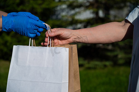 一位戴着手套的匿名志愿者将一个环保纸袋送给一位有需要的退休妇女。