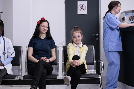 微笑的母女在繁忙的私人诊所等待儿科医生做例行检查
