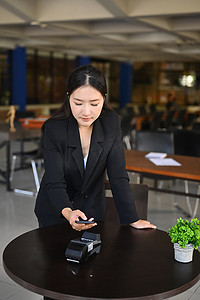 亚洲女性在咖啡店使用智能手机进行非接触式支付。