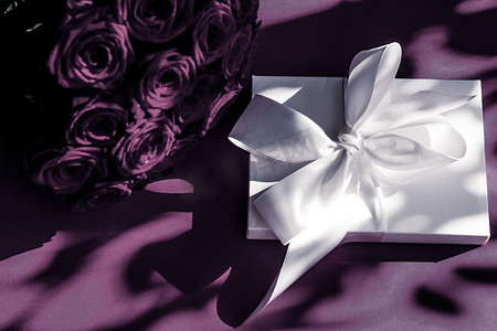 情人节紫色背景摄影照片_豪华假日丝绸礼盒和紫色背景的玫瑰花束、浪漫惊喜和鲜花作为生日或情人节礼物