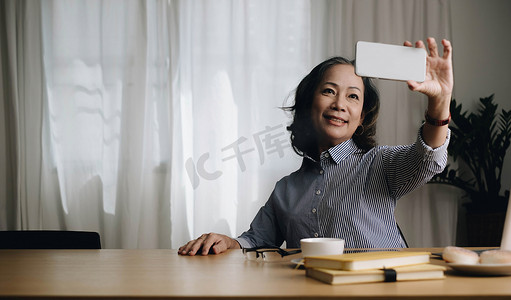 亚洲老年妇女在家里的客厅里微笑和视频通话。
