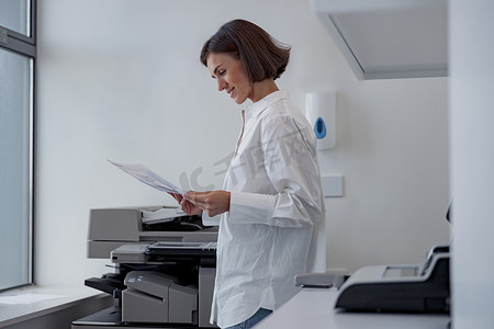 复印扫描的人摄影照片_现代办公室里微笑的女工在复印机上扫描文件