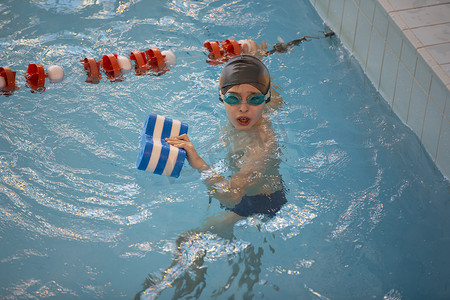 游泳池里戴着泳帽和泳镜的男孩。