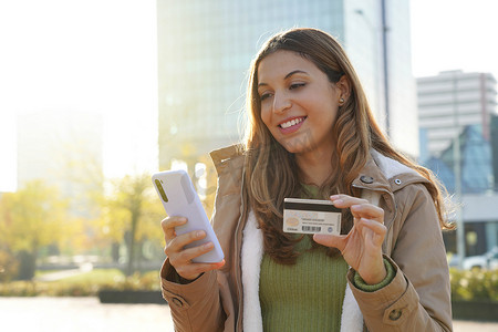 年轻女性在智能手机上输入信用卡号码的特写在网上购买或在户外支票银行账户