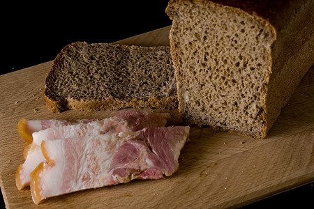 黑面包和咸猪油，黑色背景的木板上放着肉条
