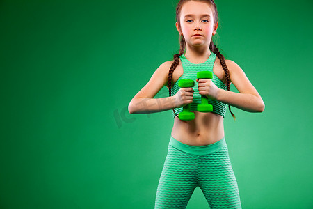 绿色背景下用哑铃做健身运动的小女孩