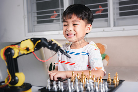 亚洲小男孩编程代码到笔记本电脑上的机器人机械臂下棋