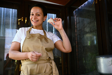 美国制作手工摄影照片_身穿厨师围裙、手里拿着发霉饺子的迷人非洲裔美国女人，喜欢烹饪乌克兰瓦列尼基烹饪课
