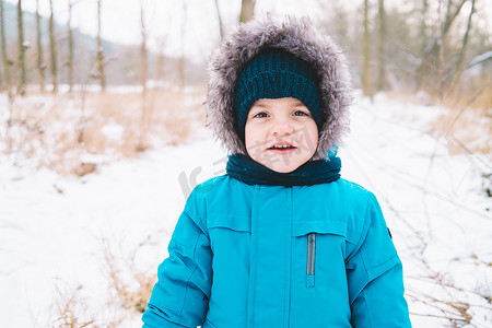 小男孩穿着冬装，戴着针织帽子，背景是雪天。