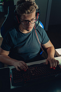 正在玩电脑的人摄影照片_年轻的金发小伙正在玩电子游戏，在屏幕照亮的黑暗中在他的笔记本电脑上玩。