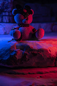 岩石背景中霓虹灯下的泰迪熊上的 bdsm 配件