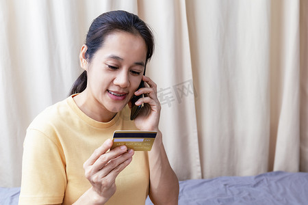 快乐的亚洲女性使用智能手机和信用卡在网上支付购物费用。