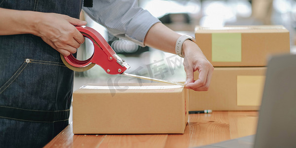 小型企业企业家 SME，亚洲年轻女性，女主人包装产品，检查包裹以交付给客户，使用透明胶带密封箱子，在家工作。