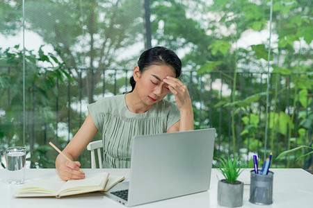 照片中，压力重重的女商人在家里用笔记本电脑工作，看上去忧心忡忡、疲惫不堪、不知所措。