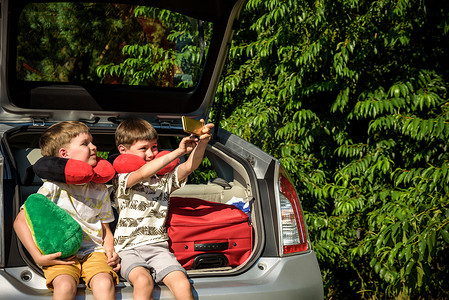 可爱小孩坐摄影照片_两个可爱的小孩男孩在离开去暑假前坐在汽车后备箱里。