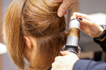 女发型师的手在美发沙龙里用卷发器给顾客卷发，特写。