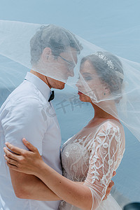 美丽的新娘和新郎在希腊圣托里尼岛的夏季婚礼当天在新娘面纱下拥抱和亲吻