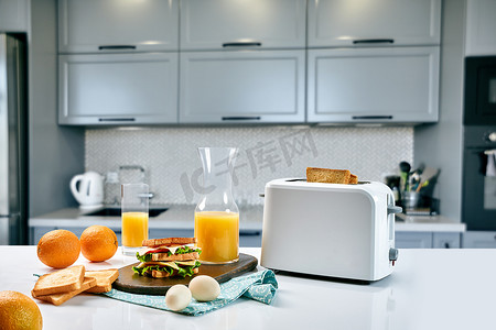白色电动面包烤面包机配橙汁和厨房桌子上的三明治。