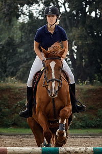 女骑手摄影照片_夏季越野比赛中骑着棕马跳过障碍的迷人女骑手特写