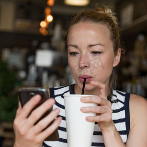 体贴的女人一边在咖啡店喝咖啡一边用手机阅读新闻。