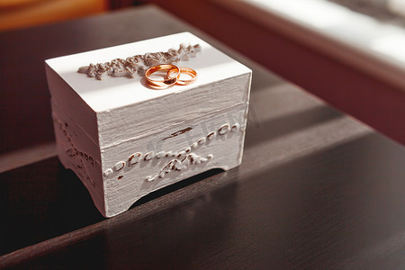 一对金色结婚戒指，白色破旧的装饰盒上镶有钻石。