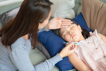 温度计发烧摄影照片_亚洲母亲用家里发烧和生病的温度计检查她孩子的体温。